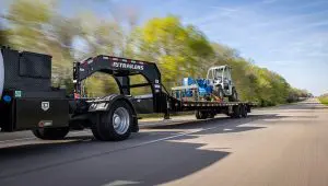 Camión con remolque Low-Pro con grúa hidráulica que transporta una carretilla elevadora de servicio pesado