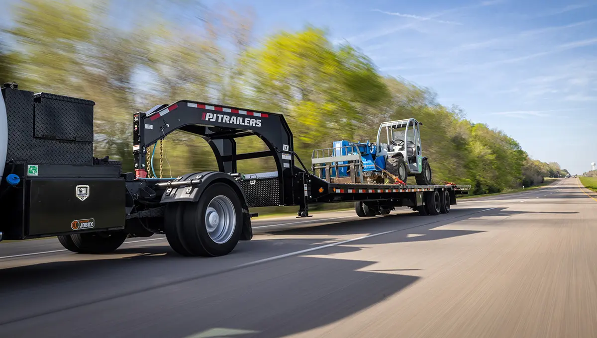 Camión con remolque Low-Pro con grúa hidráulica que transporta una carretilla elevadora de servicio pesado