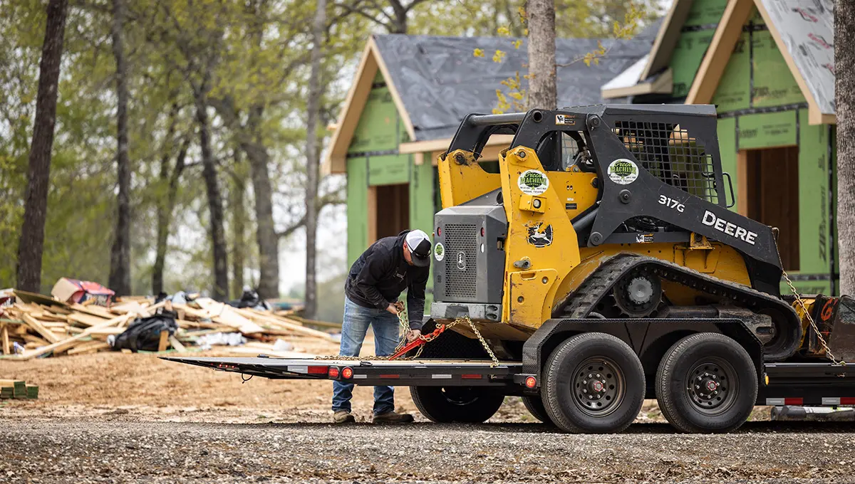 Worker securing a John Deere skid loader on the HD Equipment Tilt 6
