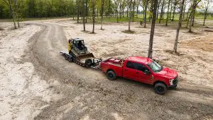 Red truck carrying a John Deere skid loader on the HD Equipment Tilt 6