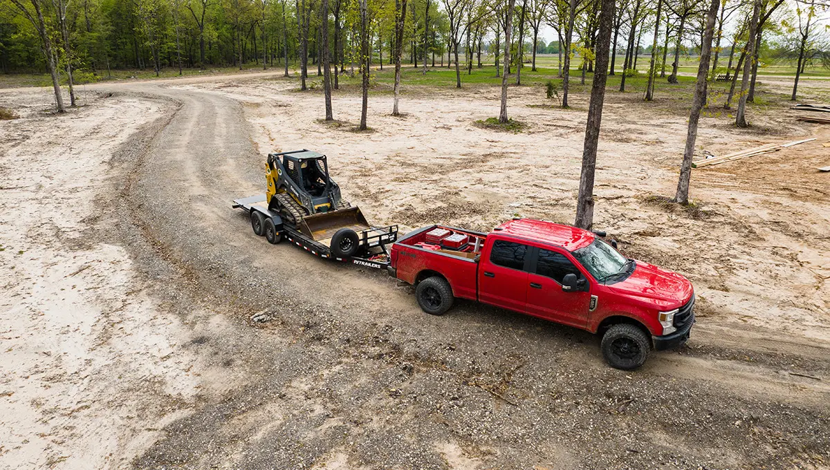 Red truck carrying a John Deere skid loader on the HD Equipment Tilt 6