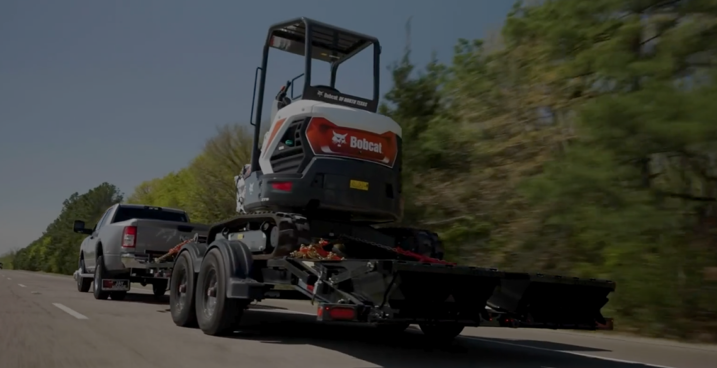 The Voyager Seamless I-Beam Equipment Trailer (EV) trailer hauling a Bobcat forklift down a highway road